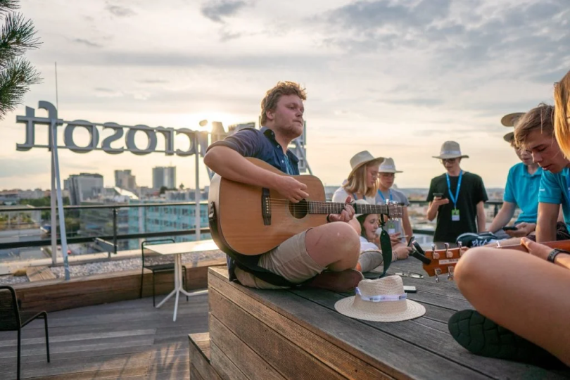 Mladý muž hraje na akustickou kytaru na střeše budovy Microsoft v Praze.